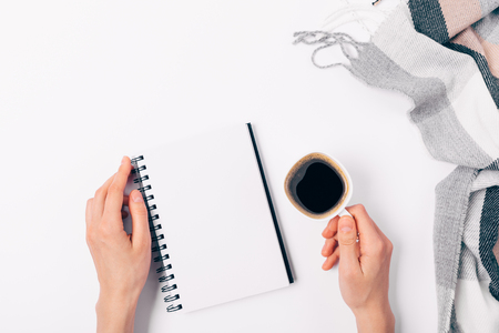 Flat lay arrangement woman's hands holding blank open notepad and cup of coffee near checkered scarf on white background, top view.の写真素材