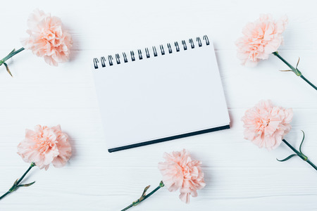 Flat layout of blank notepad among pink flowers on white table, top view.の写真素材