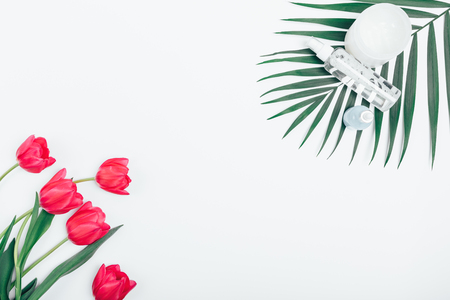 Top view cosmetics for spa treatments on palm leaf near bouquet of pink tulips on white background with an empty space in center, flat lay.の写真素材