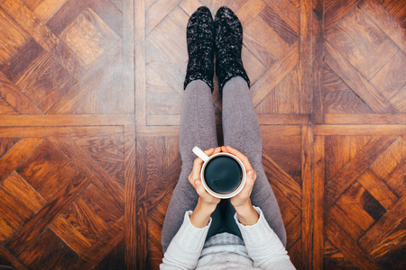 Young woman in cozy home clothes relaxing and drinking coffee sitting on the wooden floor.の写真素材