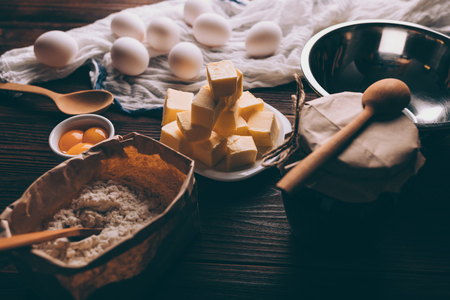 Close-up of ingredients and utensils for cooking pie on dark wooden table. Raw eggs, yolks, flour, butter and an empty bowl ready for making homemade bakery.の写真素材