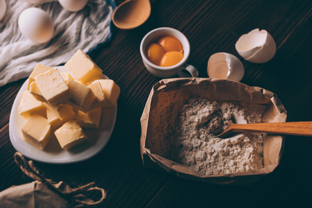 Top view of diced butter, sack of flour, raw yolks and egg shells on brown wooden table. Ingredients for baking homemade pie.の写真素材