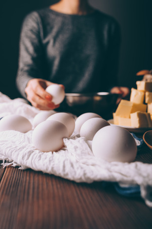 Female's hand pick egg to prepare shortcake dough for pie. Cropped image of young woman at table making homemade pastry.の写真素材