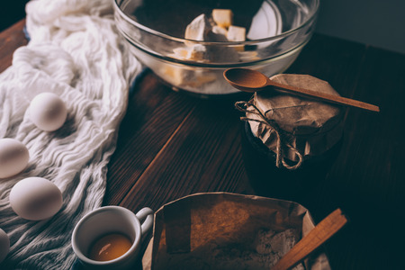 Close-up of rustic kitchen table with ingredients and utensils for cooking homemade pastry. Bowl with diced butter, bag of flour, raw eggs and jar of jam.の写真素材