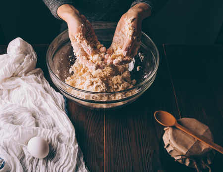 Woman's hands kneading dough in big bowl on brown wooden kitchen table. Process of cooking homemade...