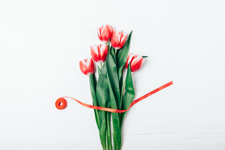 Bouquet of fresh red tulip flowers with satin ribbon on white wooden table, top view.の写真素材