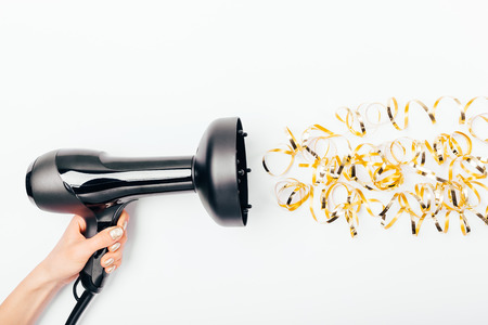 Concept of curly hair styling with special nozzle diffuser. Female hand holding hair dryer directing it to stylized golden curls on white background, flat lay.の写真素材
