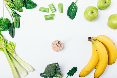 Top view of scoop of vegan protein powder among fruits and vegetables: fresh spinach, celery, broccoli, apples and bananas on white background. Flat lay frame composition of healthy eating.の写真素材