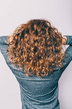 Woman's head with curly brown hair, back view. Close-up unrecognizable girl holding her haircut.の写真素材
