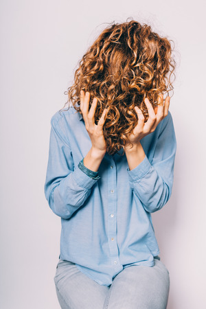 Unrecognizable young woman wearing blue shirt applying with hands a cosmetic care product on her curly hair tips.の写真素材