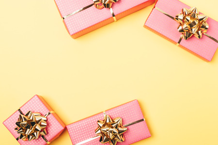 Flat lay frame of pink gift boxes with golden bows on yellow background, view from above.