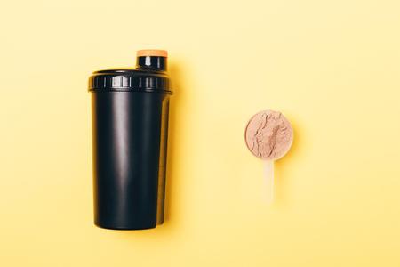Scoop of whey protein powder near shaker for sports drink on yellow background, top view.の写真素材