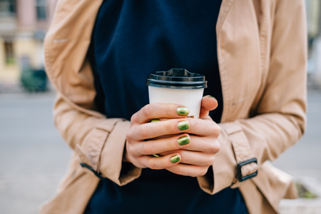 Close-up female's hands with green manicure holding cup of hot coffee outdoors.の写真素材