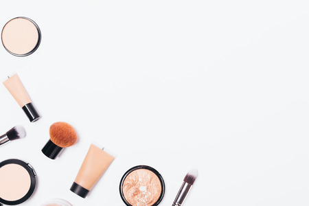 Beauty products and accessories for even complexion, top view. Flat lay frame of decorative cosmetics and makeup brushes on white background with copy space.の写真素材