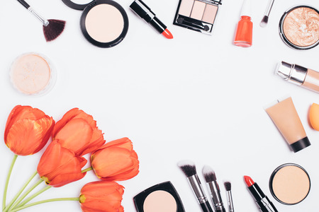 Festive flat lay composition of cosmetic products, makeup accessories and lush bouquet of flowers on white background with an empty space in center, top view.の写真素材
