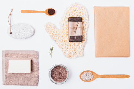 Flat layout of products and accessories for skin exfoliation and cleansing on white background. Bathroom set with coarse sisal mitten, coffee scrub with sea salt, natural soap and pumice stone.の写真素材
