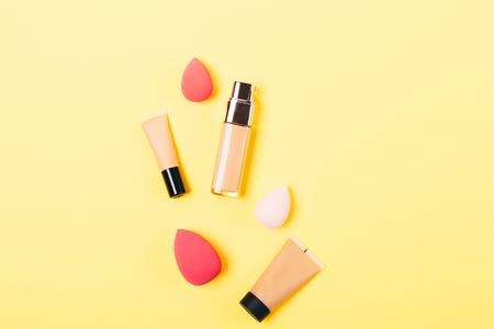 Stylish flat lay arrangement of bottles of makeup foundation next to egg shaped sponge applicators, top view on yellow background.の写真素材
