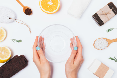 Woman's hands holding empty glass bowl to make homemade bath body scrub of coffee, sea salt with rosemary and fresh citrus lemon and orange, flat lay composition on white background.の写真素材