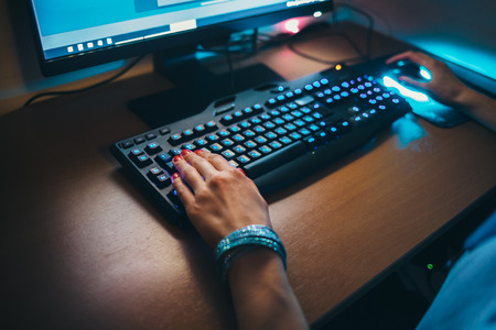 Close-up of female hands typing on keyboard and holding mouse with led backlight. Young woman working at home on personal computer sitting at table during night.の写真素材