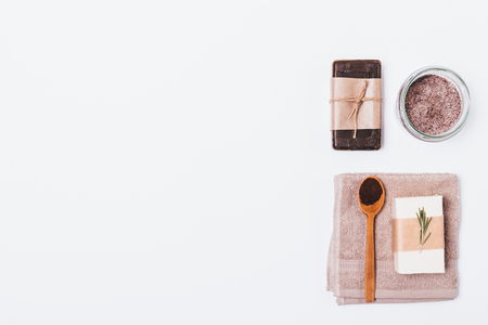 Flat lay composition of coffee cosmetics for cleansing and exfoliating skin at home. Organic soap, scrub of ground coffee and sea salt with rosemary oil on white background with empty space for text.の写真素材