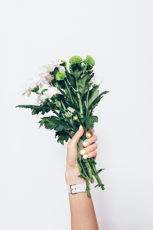 Female hand holding fresh green bouquet of flowers on white background, close-up.の写真素材