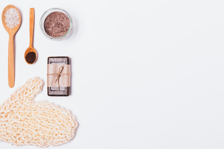 Bath background of coarse washcloth, soap and coffee scrub with sea salt, flat lay. Natural cosmetic products and accessories for cleansing and exfoliating dead skin cells on white table, top view.の写真素材