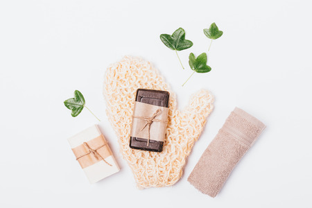 Natural accessories and bath soap next to green leaves on white background, flat lay decorative composition.の写真素材