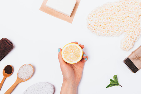 Anti-cellulite natural cosmetics and accessories on white background, flat lay. Top view of female's hand holding a sliced lemon next to ingredients for coffee body scrub and massage sponge.の写真素材