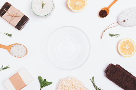 Flat lay arrangement of empty glass bowl next to ingredients for homemade bath body scrub of coffee, sea salt, rosemary, mint and fresh lemon on white background.の写真素材