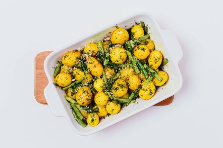 Top view ceramic baking pan baked new potatoes with green beans, garlic and dill, sprinkled with almond crumbles on white table.の写真素材
