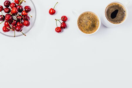 Flat lay frame of coffee and berries healthy snack on white background with copy space. Top view two cups of espresso and bowl of cherries.の写真素材