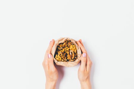 Flat lay arrangement of female hands holding open brown paper bag with walnuts on white background.の写真素材
