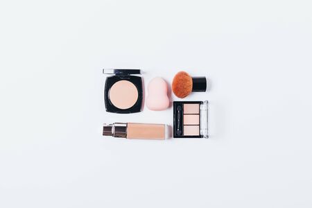 Set of makeup products to create smooth complexion, foundation, sponge blender, powder and brush next to palette of natural eyeshadow, flat lay on white background.の写真素材