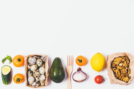 Top view frame border of wholesome food as vegetables, quail eggs, nuts and avocado on white...