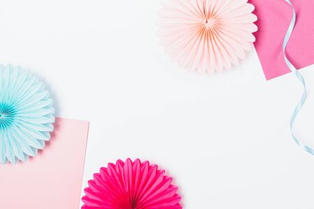Flat lay frame of paper party decorations of pink and blue colors on white background with free space in center.