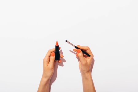 Top view woman's hands with manicure holding classic red lipstick and thin brush for applying on white background.の写真素材