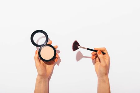 Female hands holding pressed powder and makeup brush on white background, flat lay concept composition with hard light.の写真素材
