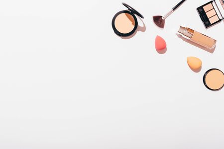 Makeup background of powders, foundation, eyeshadow with professional applicators sponges and brushes on white table with copy space.の写真素材