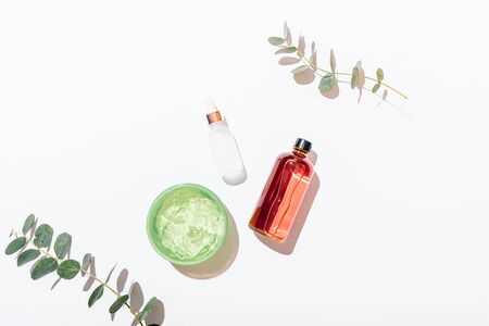 Flat lay arrangement homemade organic cosmetics facial moisturizing lotion, serum and aloe vera gel next to eucalyptus branches on white table, top view.の写真素材