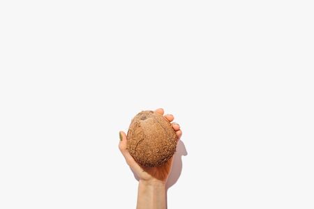 Minimal flat lay composition of female hand holding one coconut on white background, view from...