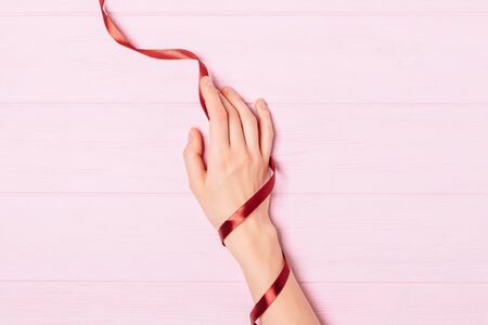 Top view woman's hand wrapped in red silk ribbon on a pink wooden table, flat lay.の写真素材