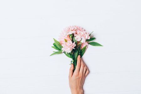 Woman's hand holding beautiful bouquet of pale pink carnation flowers on white background, flat lay.の写真素材