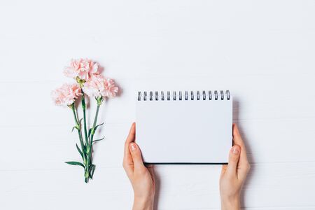 Empty notepad mockup in female hands next to bouquet of fresh flowers on white background, flat lay.の写真素材