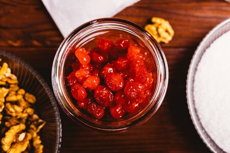 Top view of dried cherry berries in glass jar next to walnuts on brown wooden table, close-up.の写真素材
