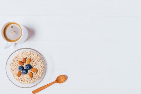 Bowl of oatmeal with nuts and berries next to cup of freshly brewed coffee as healthy breakfast on white wooden background with copy space, top view.の写真素材