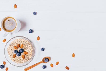 Healthy balanced breakfast of oatmeal with blueberries and almonds next to black coffee on white wooden background with copy space.の写真素材