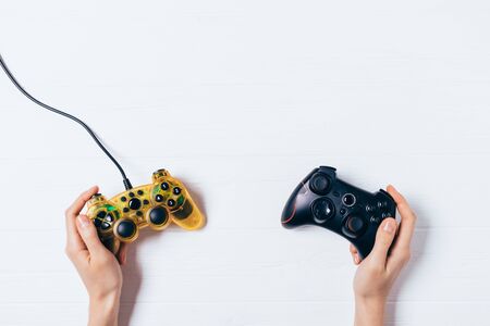 Female hands holding two gamepads on white wooden background, flat lay composition.の写真素材