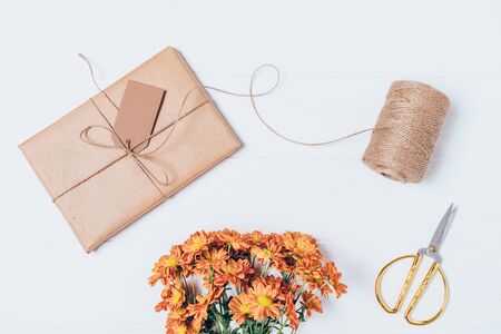 Handmade packed gift box next to scissors, jute rope and a festive bouquet of flowers on white table, top view.の写真素材