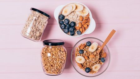 Wholesome homemade food flat lay. Top view oatmeal and granola breakfast in bowls and jars for storage on pink tableの写真素材