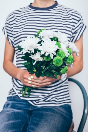 Close-up young woman holding bouquet of fresh flowers sitting on white studio background.の写真素材